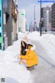 A woman in a yellow coat crouching down in the snow.