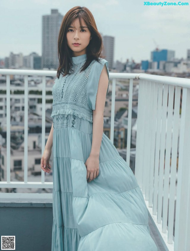 A woman in a blue dress standing on a balcony.