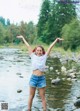 A woman standing in a river with her arms outstretched.