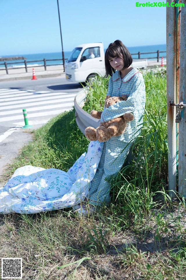 A woman sitting on the side of a road holding a teddy bear.