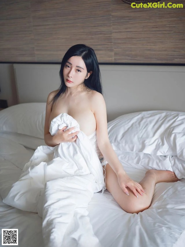 A woman sitting on top of a bed covered in white sheets.