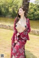 A woman in a red kimono posing next to a tree.