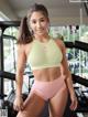 A woman in a green sports bra top and pink shorts posing in a gym.